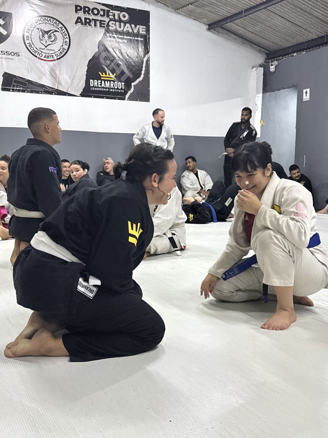 A coach in a black gi helping a student at Projeto Arte Suave