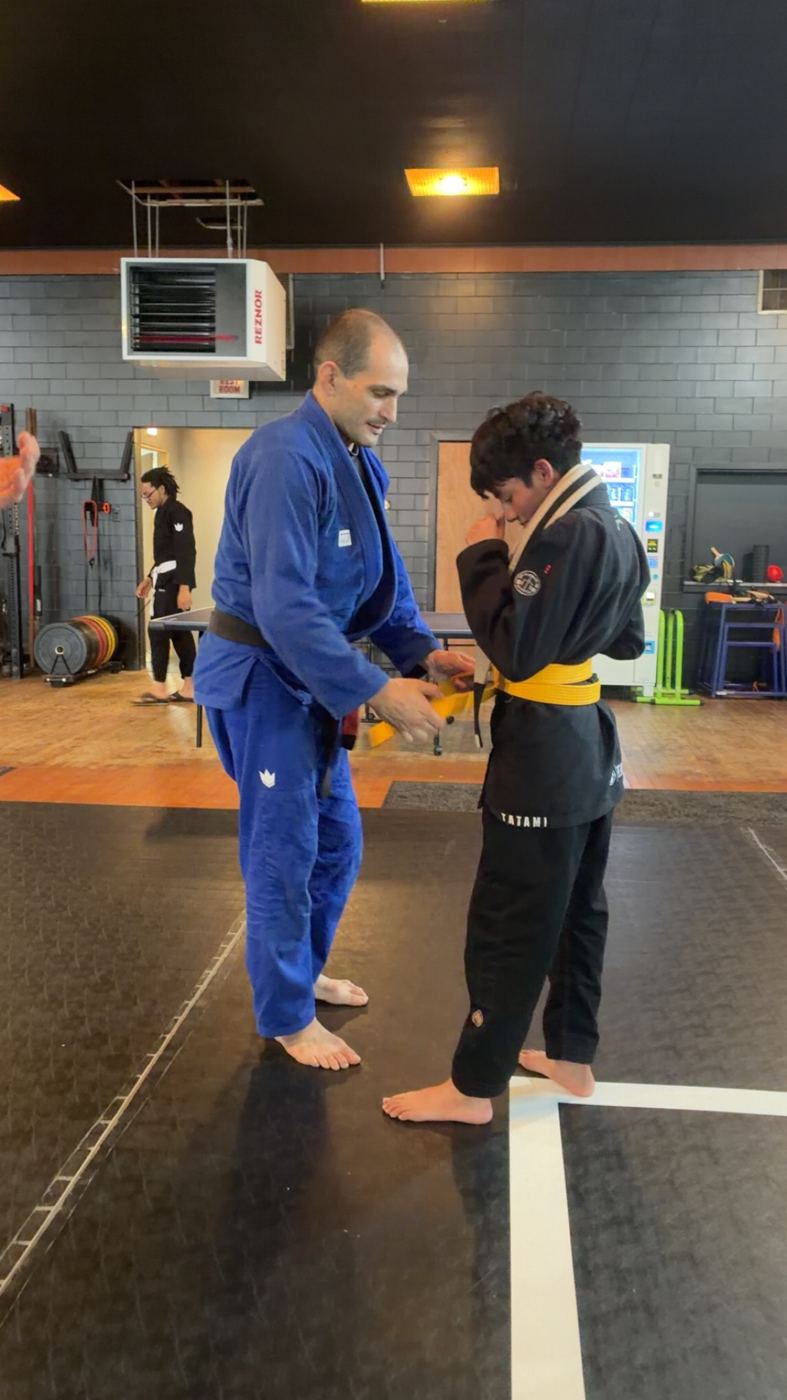Coach tying a new yellow belt on a kids student