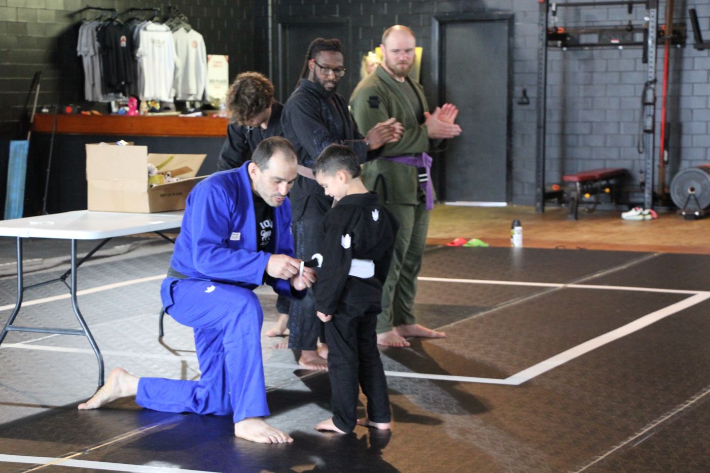 Coach kneeling to award a stripe to a young student while coaches clap